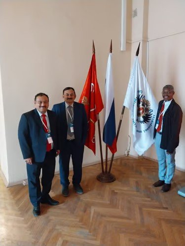 Prof. Sijariya with two colleagues in front of ceremonial flags